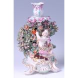 An 18th century Derby porcelain candle-holder, modelled as Cupid against a floral bocage,