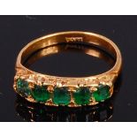 An 18ct gold and emerald set dress ring arranged as five graduated emeralds in a chased line