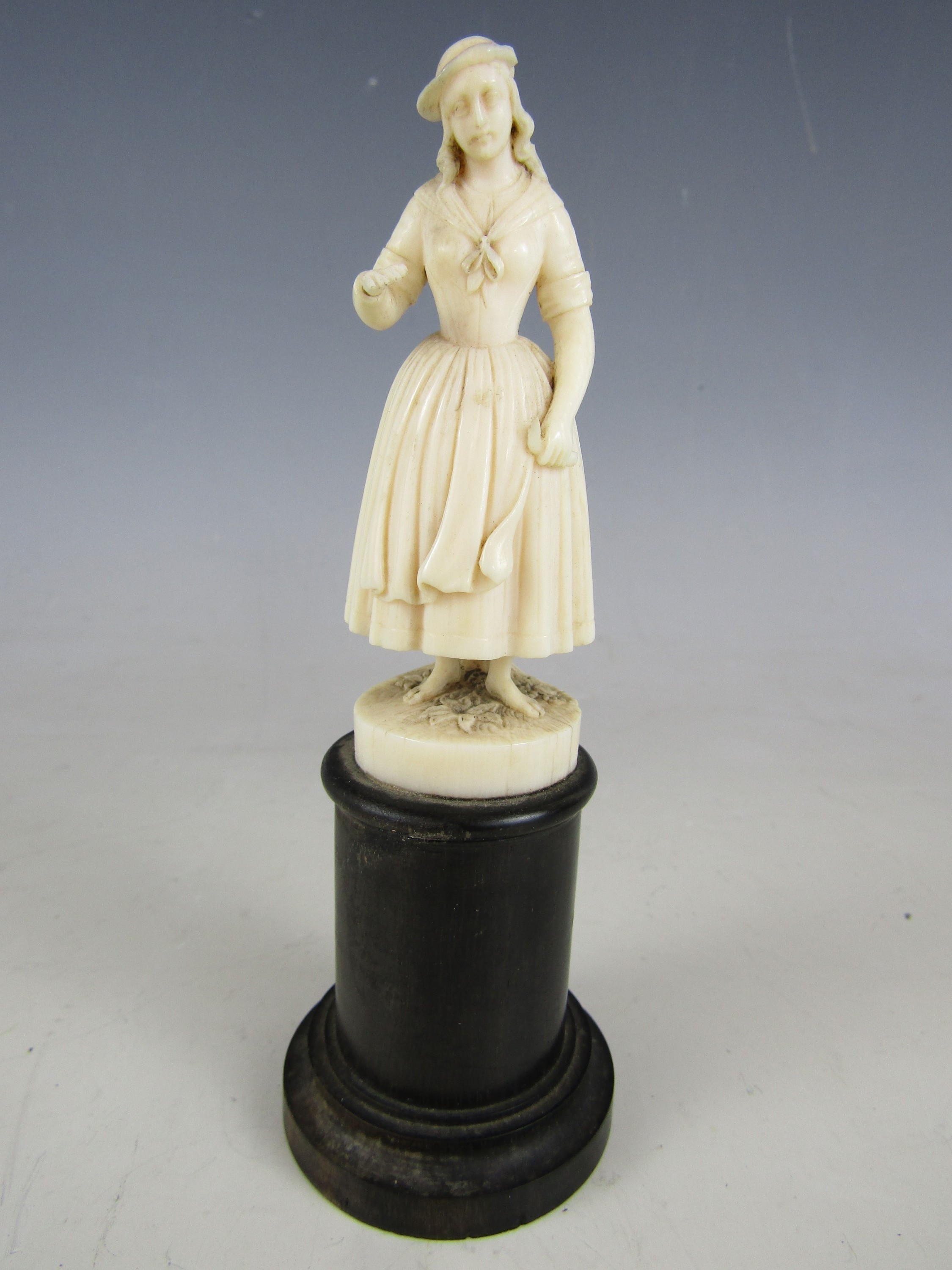 A finely carved ivory statuette of an 18th Century peasant girl, on a turned ebony socle, 19th