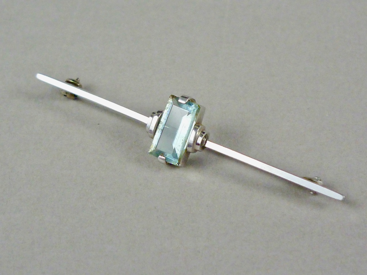 A vintage Art Deco style white-metal bar brooch centrally set with a baguette cut aquamarine,