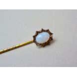 A yellow-metal and opal stick pin, the cabochon pellet-set within a cusped frame