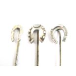 Three white metal stick pins each with a lucky horseshoe terminal, test as silver, 3.7g total