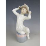 A Lladro figurine of a young girl trying on a summer bonnet