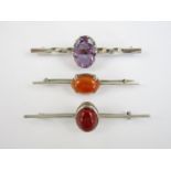 Three silver and white metal bar brooches, each centrally set with a faceted or polished stone