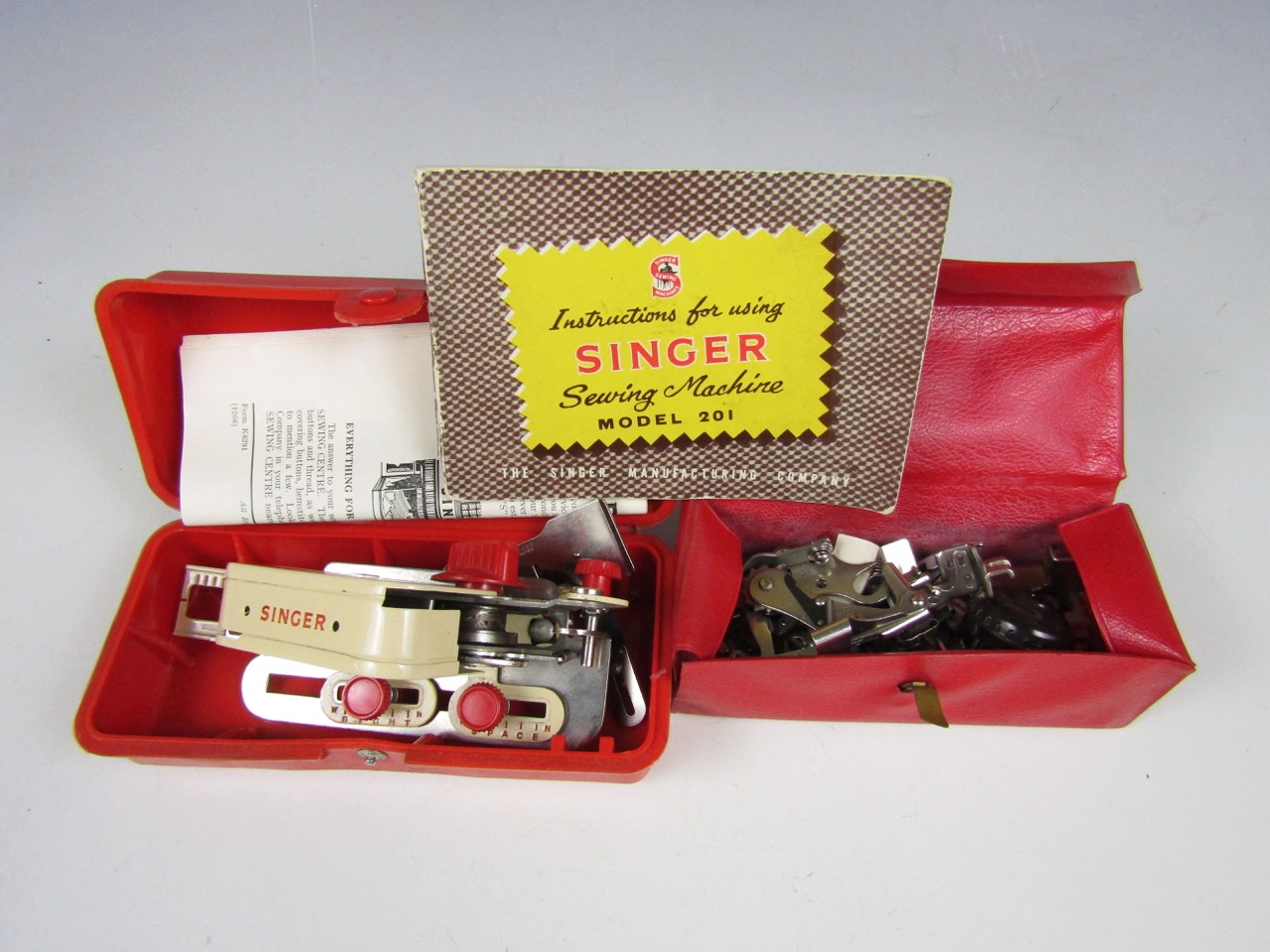 A vintage cased Singer buttonhole attachment implement together with Singer attachments and