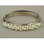 A seed pearl and silver hinged bangle, decoratively engraved and set to the face with threaded