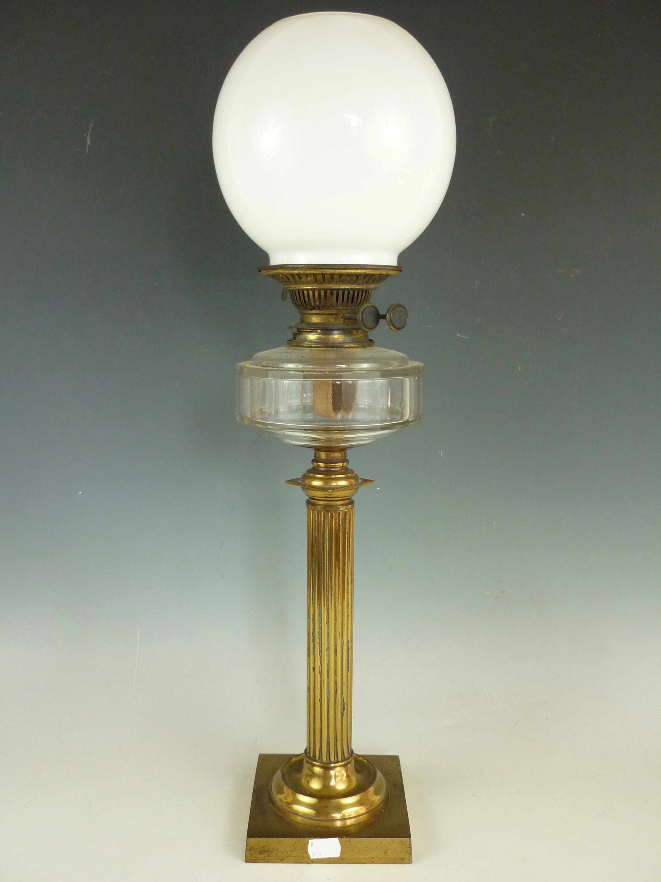 A 19th Century lacquered brass columnar oil lamp, with clear glass reservoir and milk glass shade,