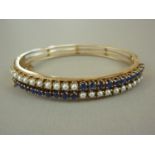 A high-carat yellow metal sapphire and pearl hinged bangle, the face claw-set with adorsed