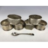 Four silver napkin rings together with two white metal napkin rings and a silver spoon