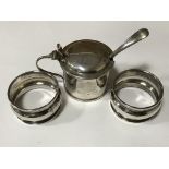 A silver mustard pot with spoon together with two silver napkin rings