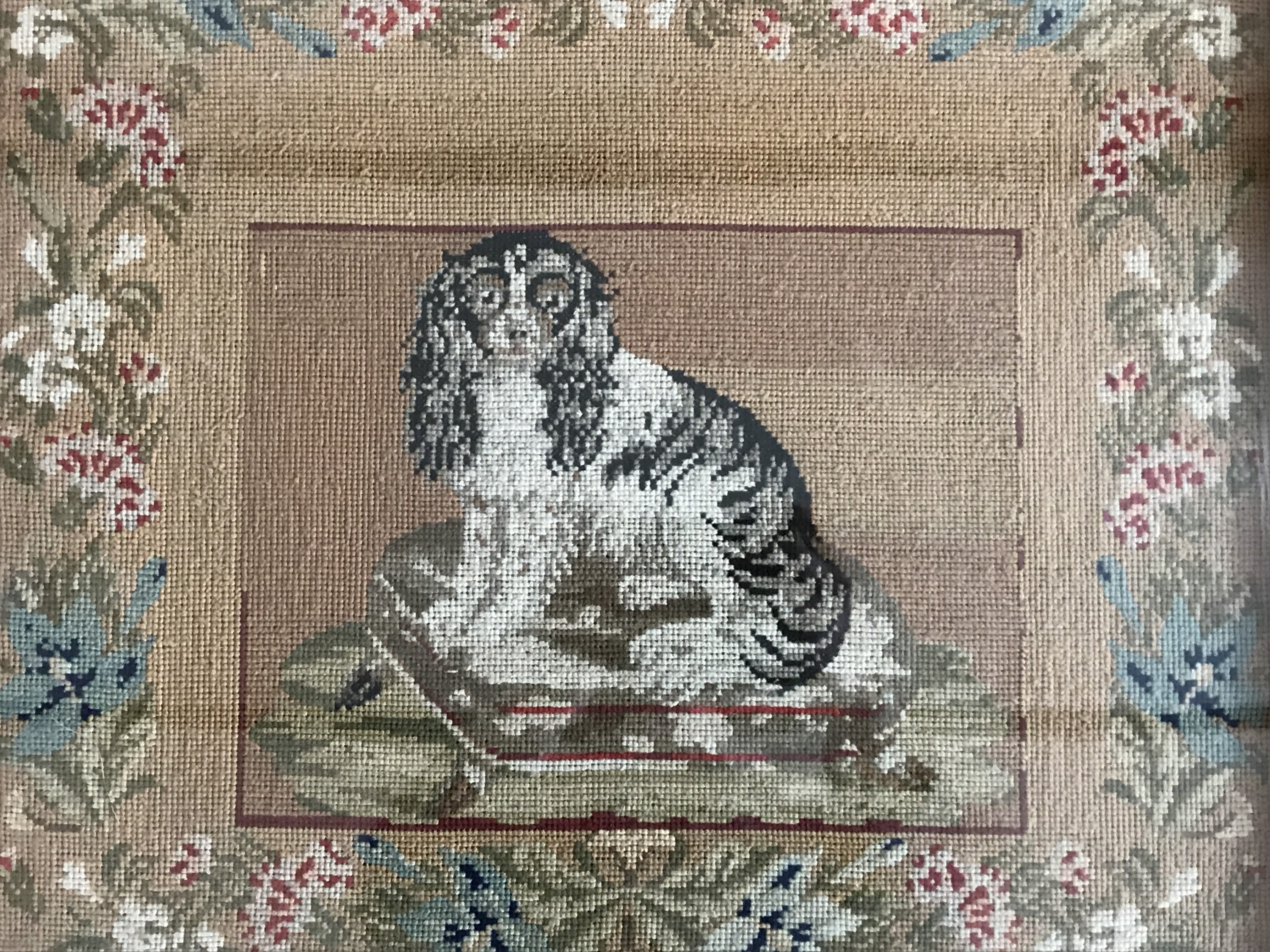 A Victorian woolwork gros point embroidery of a spaniel seated on a footstool, in a running floral - Image 2 of 2