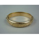A 9ct gold hinged bangle, the face engraved with three floral sprigs over a textured ground, 32.6g