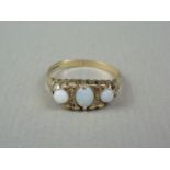 A three-stone opal ring, the opal cabochons divided by pairs of small diamonds, claw-set on 9ct