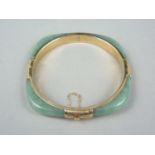 A high carat yellow metal and jade bangle, of rounded square section, mounted to each face with an