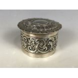 A Victorian silver trinket box, of cylindrical form with slip lid and flange rim, bearing repousse-
