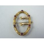 A Victorian garnet and yellow metal brooch in the form of a buckle, the faceted stones millegrain