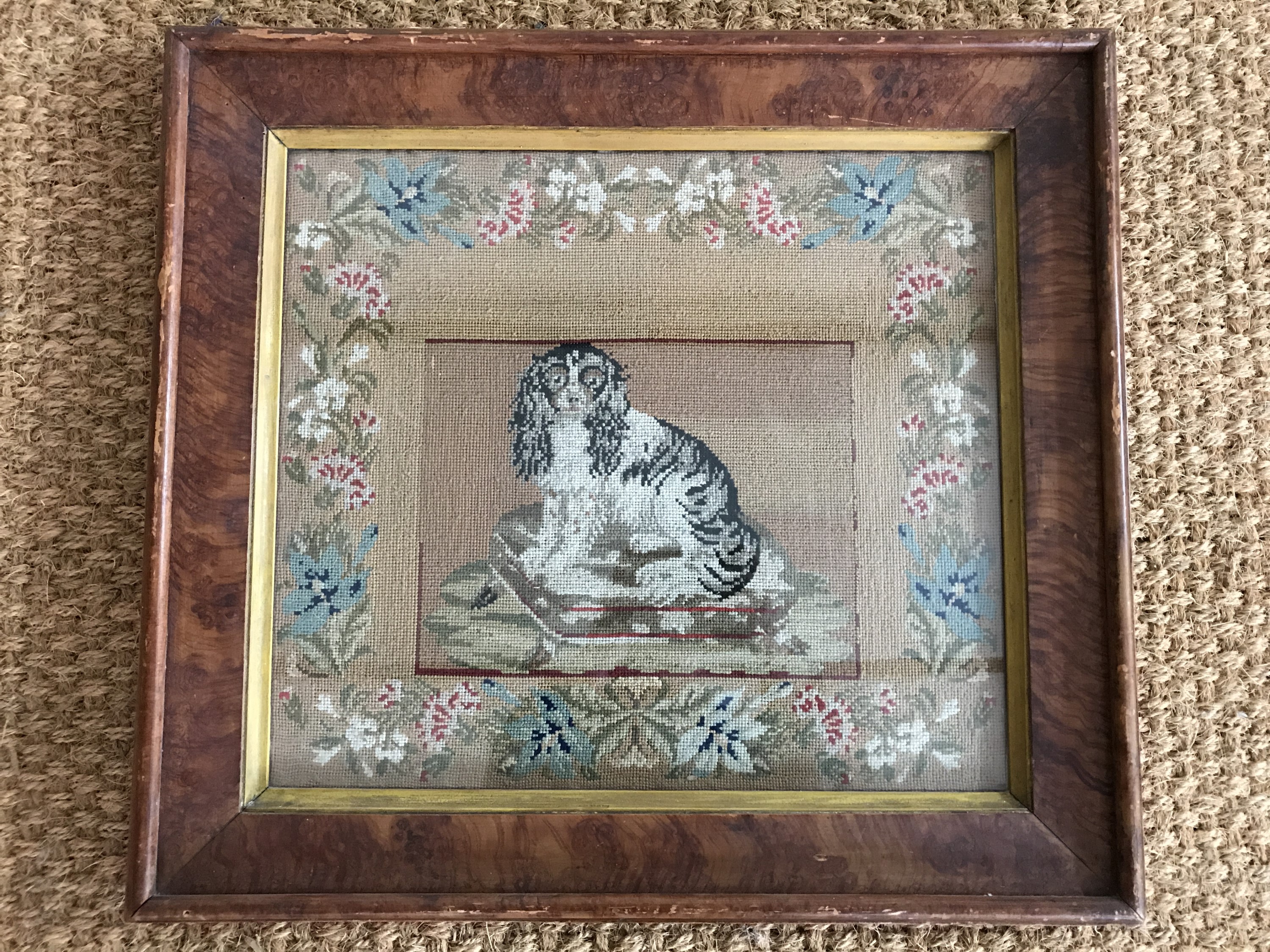 A Victorian woolwork gros point embroidery of a spaniel seated on a footstool, in a running floral