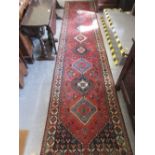 Indo Persian runner with repeating hooked medallion design on a red ground with borders,