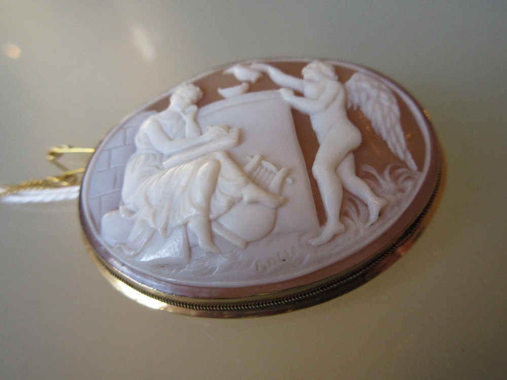 Oval shell cameo brooch carved with figures before a plinth,