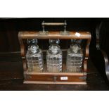 Early 20th Century oak three bottle tantalus with cut glass decanters