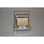 Silver stationery rack incorporating a perpetual calendar on a rectangular base with shaped feet