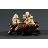 TWO JAPANESE IVORY NETSUKE, of demons appearing from a box and a seated figure, on a hard wood