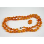 A SINGLE ROW GRADUATED AMBER BEAD NECKLACE 100cm. long, 83.2 grams, together with an amber oval-