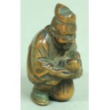 JAPANESE WOODEN NETSUKE OF A MAN CARRYING A BABY, resting on one knee, with carved swastika