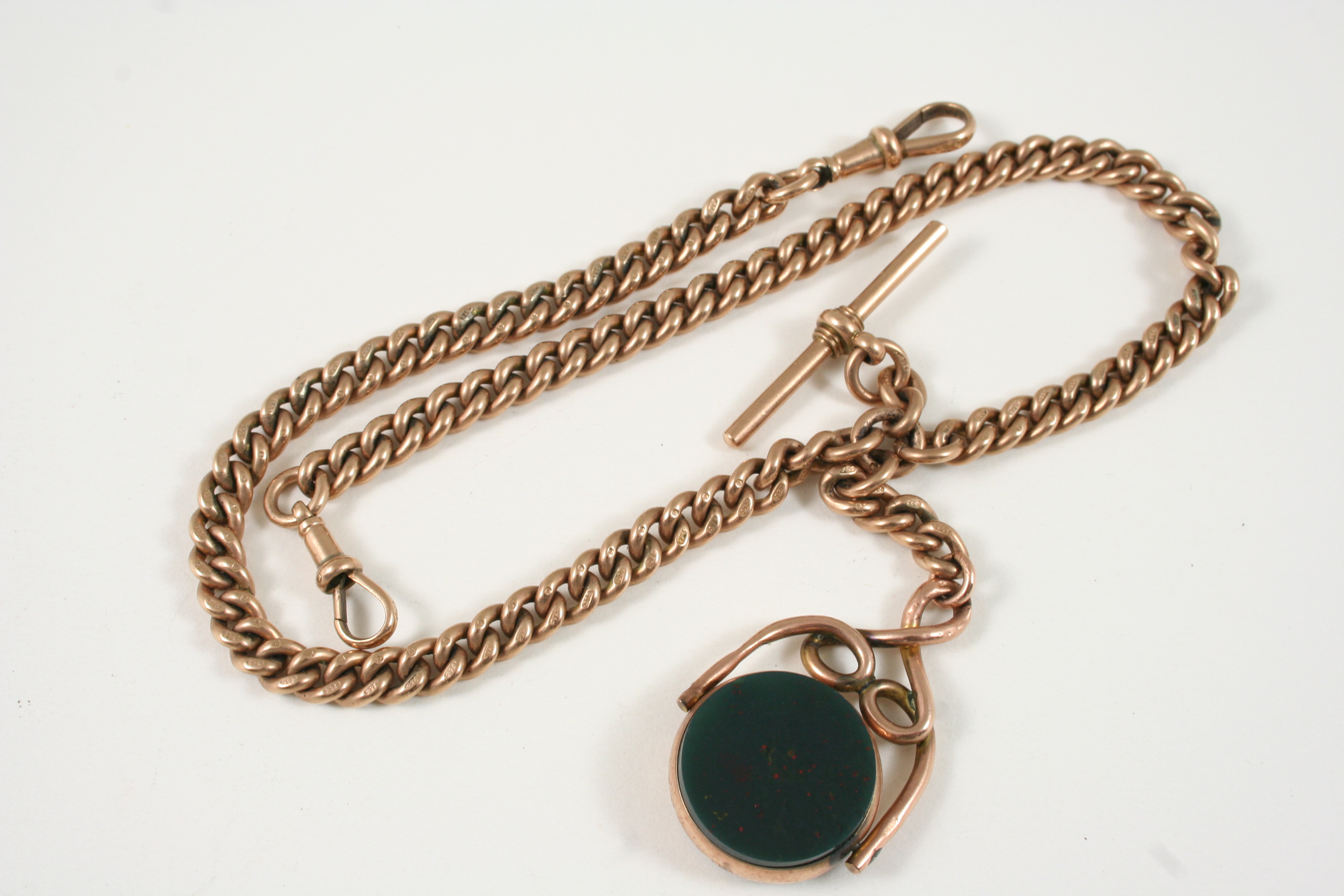 A 9CT. GOLD CURB LINK WATCH CHAIN suspending a gold 't' bar and a gold spinning fob set with a