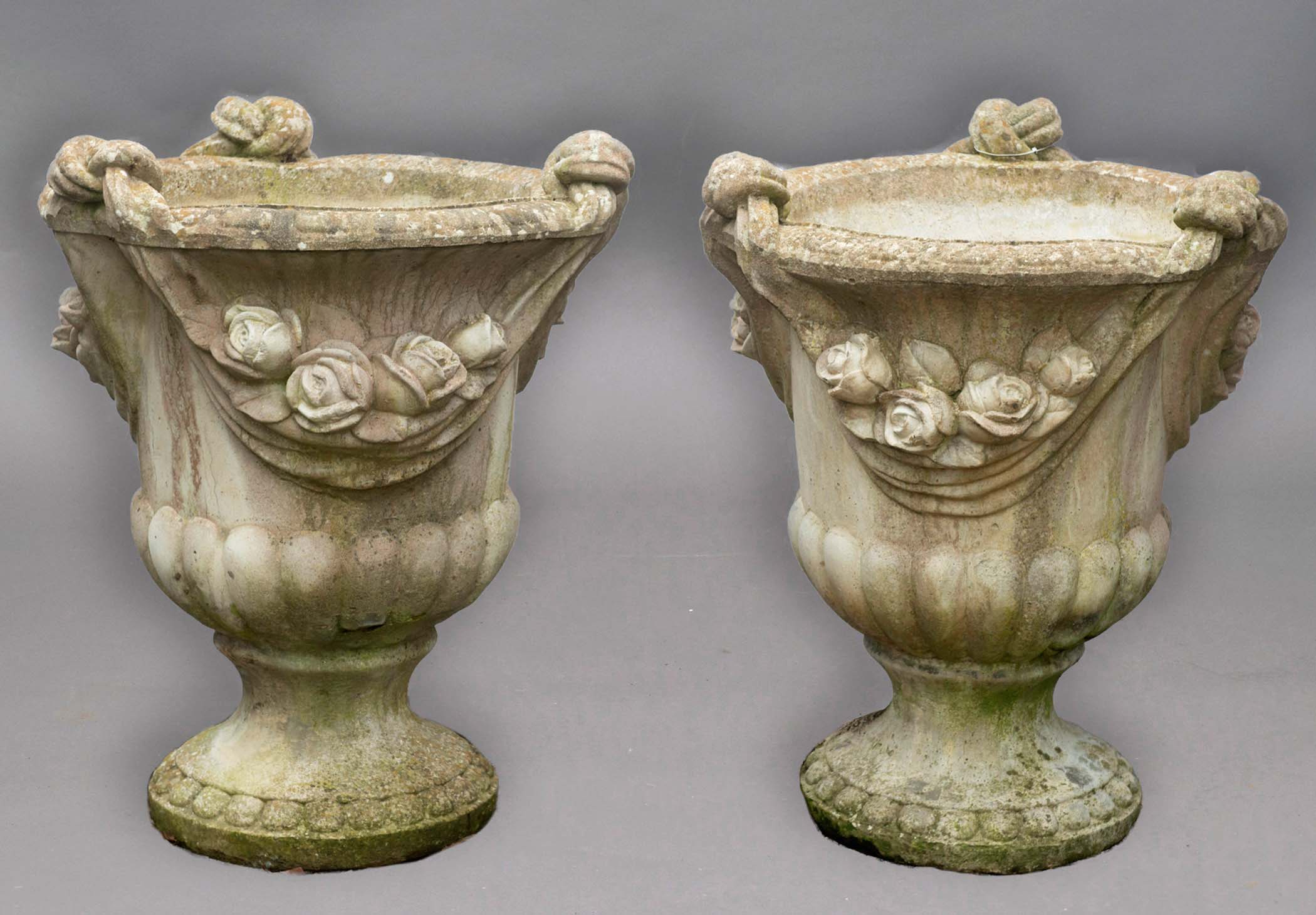 PAIR OF RECONSTITUTED STONE URNS, of campana form cast in high relief with knotted swags above