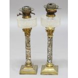 NEAR PAIR OF OIL LAMPS, the moulded glass reservoirs above 'agate' stoneware and brass mounted