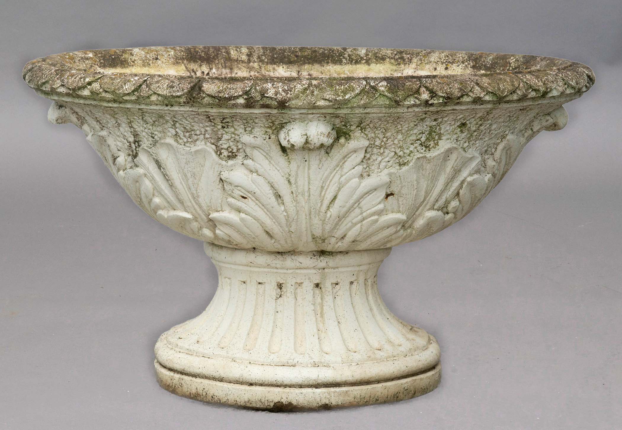 OVAL RECONSTITUTED STONE URN, with stiff leaf rim, foliate body and fluted socle base, length 100cm