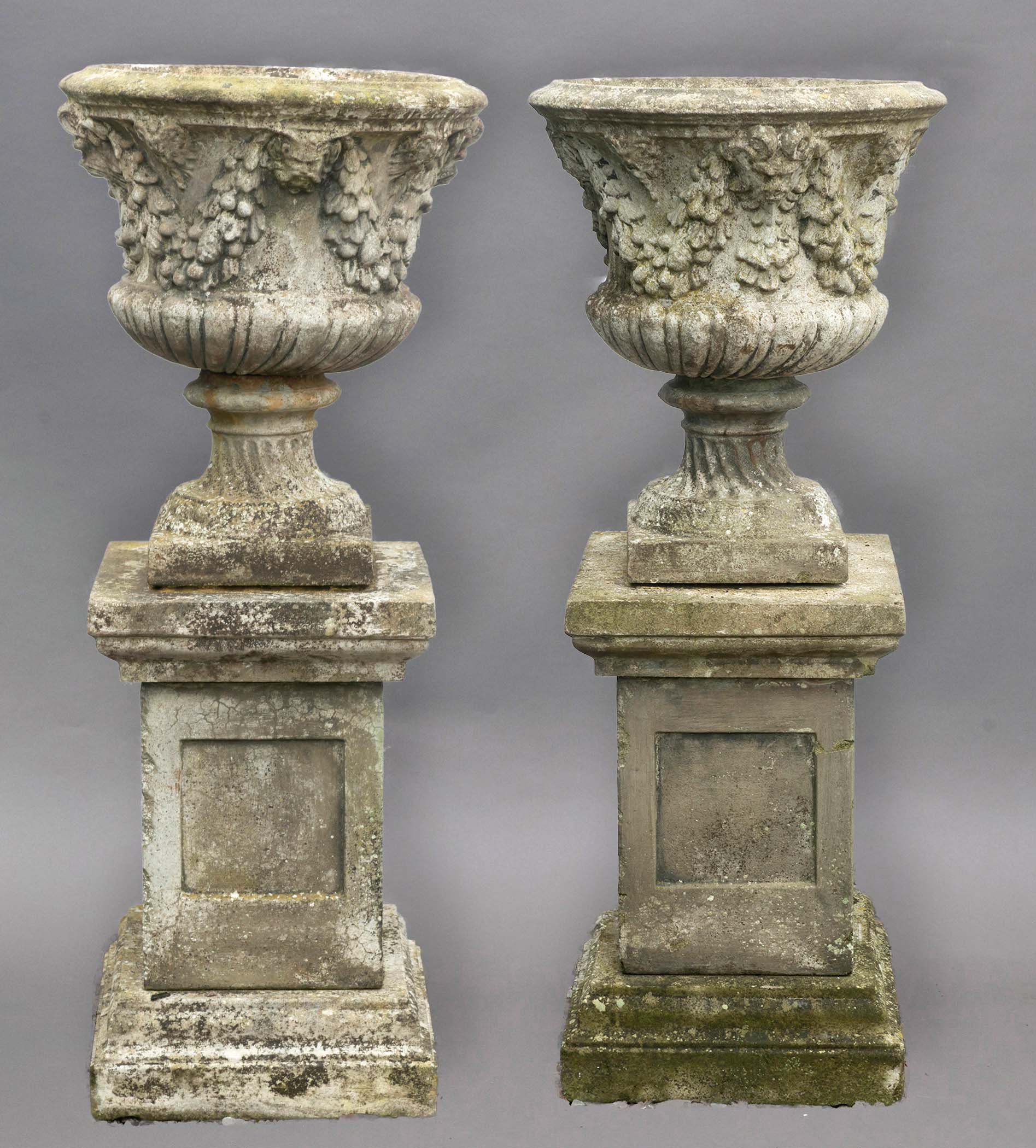 PAIR OF RECONSTITUTED STONE URNS ON PEDESTALS, with mask and foliate swag decoration on wrythen