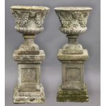 PAIR OF RECONSTITUTED STONE URNS ON PEDESTALS, with mask and foliate swag decoration on wrythen