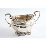 AN EDWARDIAN TWO-HANDLED SUGAR BOWL of shaped oval outline with ornate pierced feet and a decorative