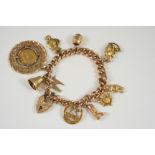A 9CT. GOLD CURB LINK BRACELET with foliate engraved padlock clasp and suspending assorted charms,