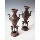 A pair of late 19th century Japanese bronze twin handled urns, cast in shallow relief with long