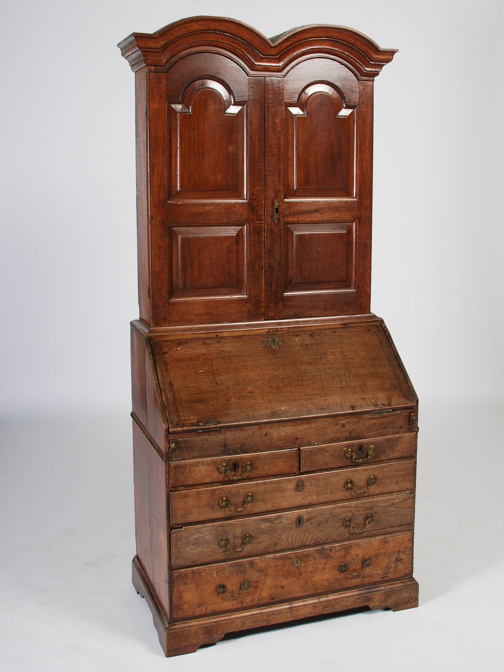 A George III oak bureau bookcase, the double domed moulded cornice above a pair of panelled cupboard