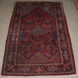 A Kashan rug, the central rectangular madder ground field decorated with urns issuing flowers, bowls