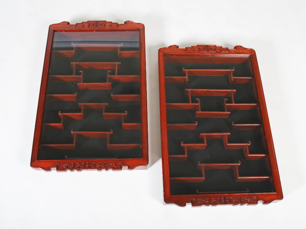 A pair of Chinese dark wood wall mounted display cabinets, the glazed cupboard doors opening to