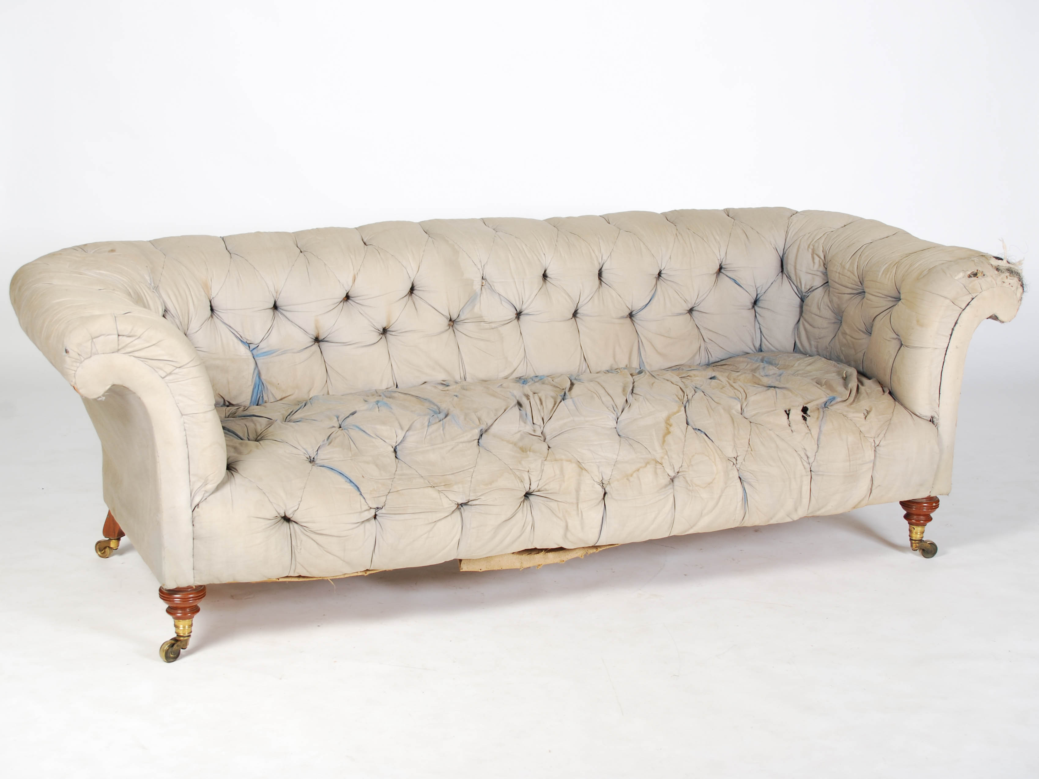 A Howard & Sons walnut Chesterfield sofa, raised on turned supports with brass cups and castors,