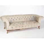 A Howard & Sons walnut Chesterfield sofa, raised on turned supports with brass cups and castors,