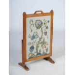 A carved oak fire screen by Beaverman, the hinged rectangular screen with needlework upholstered