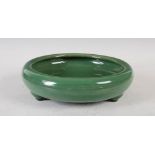 A Chinese monochrome green glazed shallow bowl, Qing Dynasty, raised on three tapered cylindrical