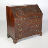 A later carved George III oak bureau, the hinged fall front carved with figural panel depicting