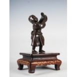 A Miyao bronze figure of a boy standing beating a drum, Meiji Period, on carved wood stand with