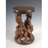 An African carved wood tribal stool, the circular top supported by two figures sitting on