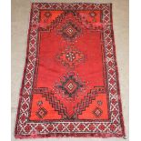 An Eastern rug, the madder ground centred with three lozenge shaped panels within a border of