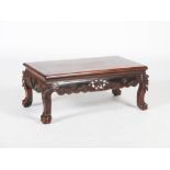 A Chinese dark wood low table, Qing Dynasty, the rectangular panelled top above a scroll and foliate