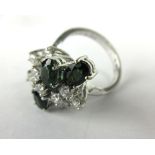 An 18ct white gold ring set nine small diamonds and four oval emeralds in a prunt-type spray